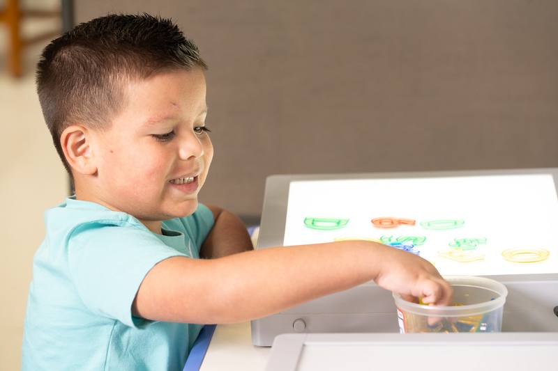 A Pasadena student practicing letters at a light table